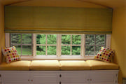 The soft green roman shade and yellow cushions make this window seat an inviting place.
