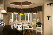 Bay window with a box pleated valance with silk plaid band mounted over linen drapes with iron tiebacks
