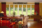 The red and gold damask drapes with the silk roman shades and striped  window seat draw their inspiration from the red leather sofa.
